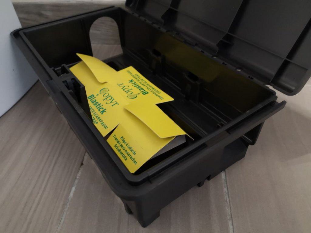 Contenitore nero aperto con trappola collante gialla Copyr Blastick per scarafaggi, su pavimento in gres effetto legno